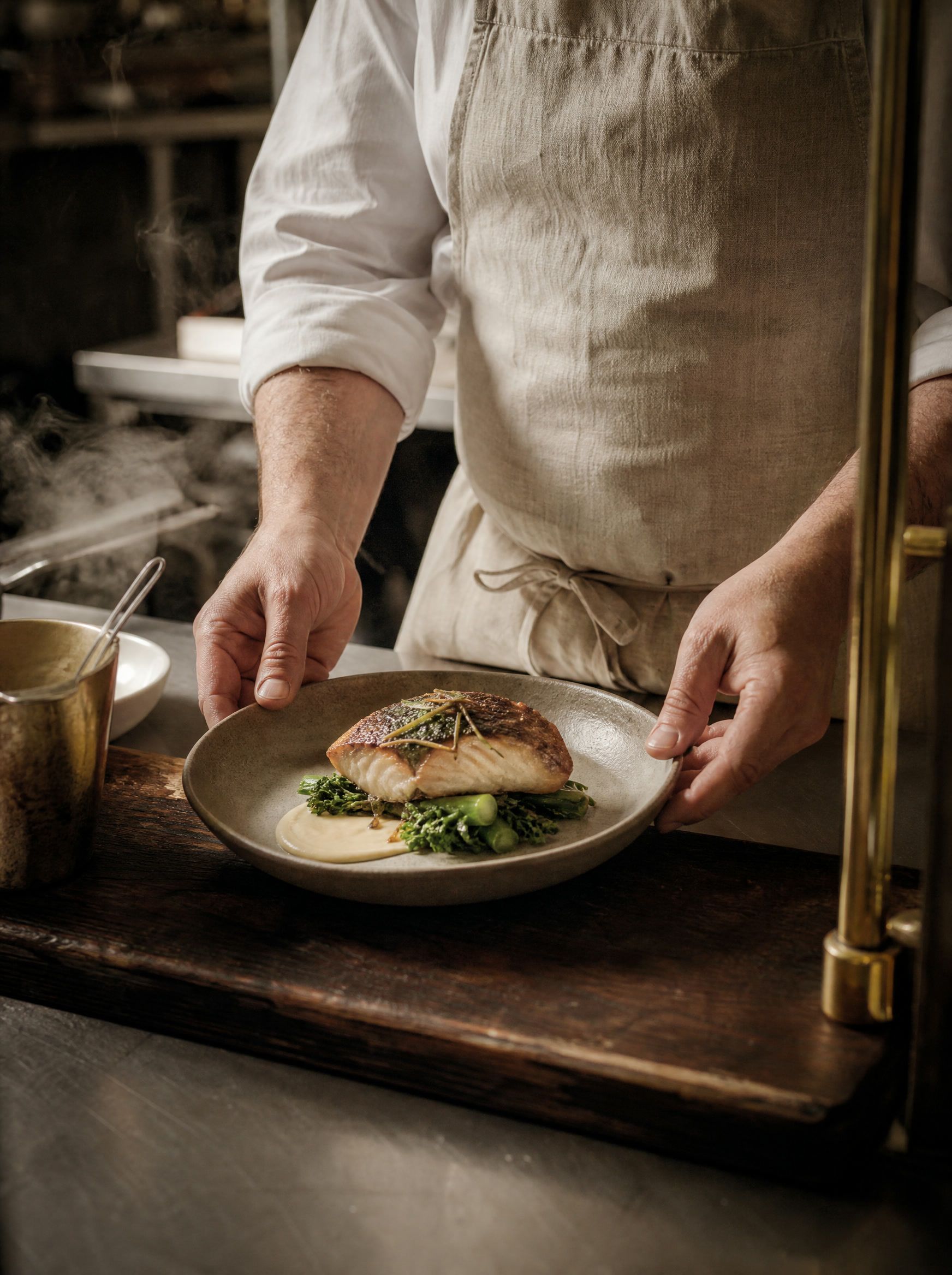 A chef's hands placing a plated dish of seared fish on a stoneware plate at the pass